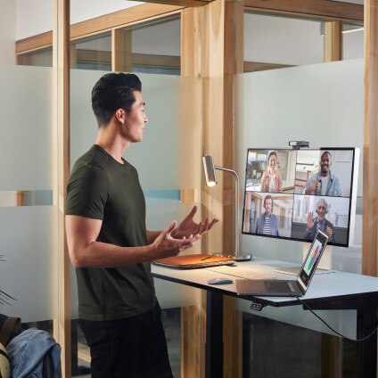 Colleagues in a meeting room video conference with other colleagues who appear on the screen mounted on the wall.