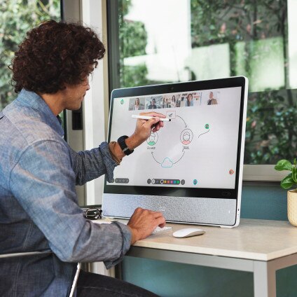 Person in a headset video conferences from his laptop in his office. Skyscrapers are seen outside  the window.